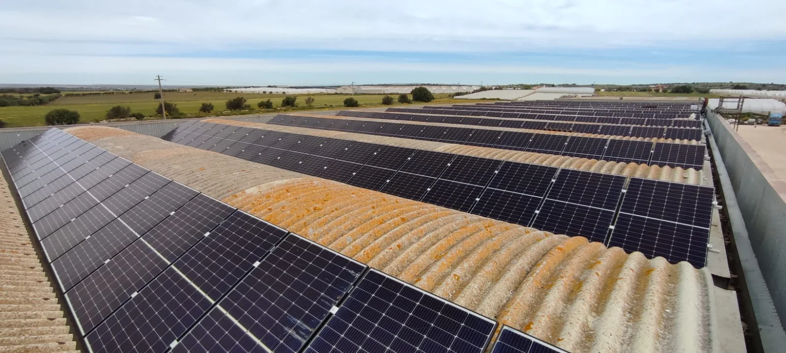 Impianto fotovoltaico su ampia copertura: file di moduli allineati sulla falda sotto un cielo terso — generazione da fonte solare per l'efficienza energetica