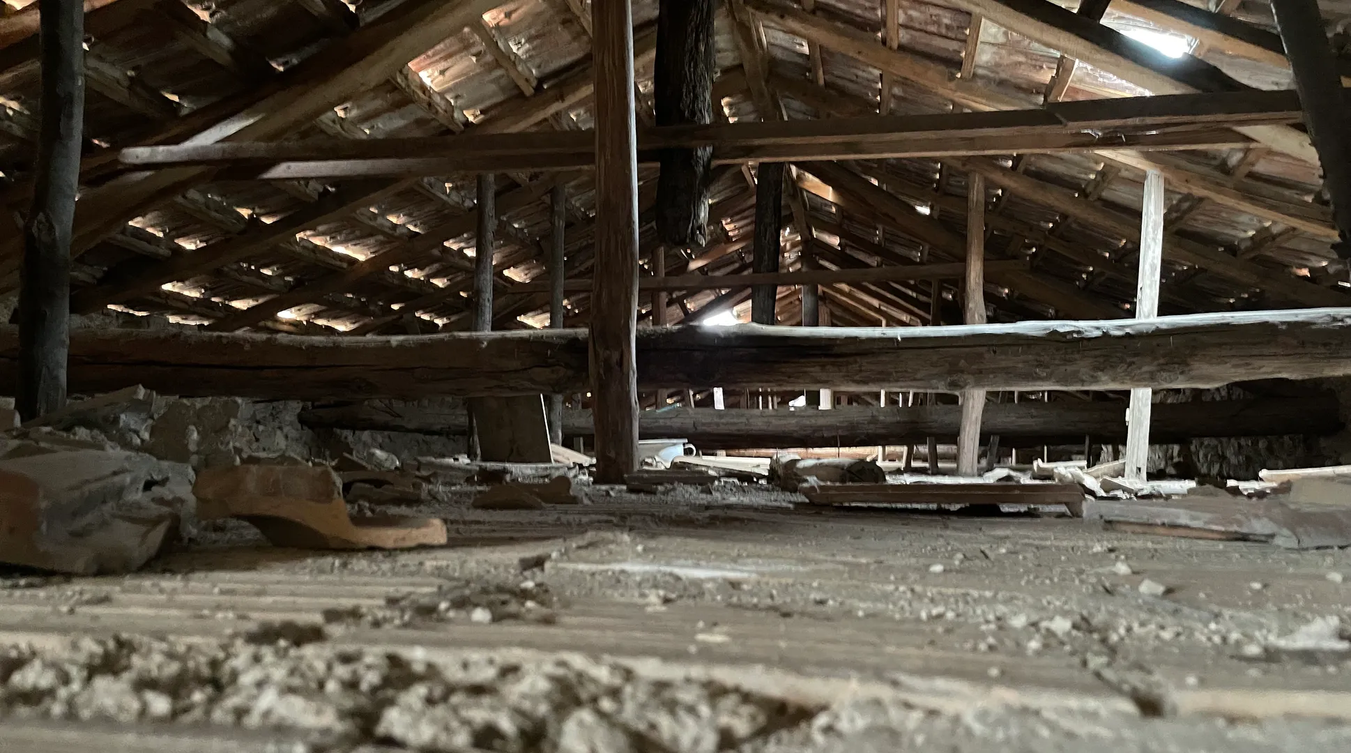 Sottotetto di un edificio storico: orditura lignea del tetto con capriate, arcarecci e pianelle in cotto a vista, e solaio sottostante con detriti — rilievo strutturale su edificio esistente